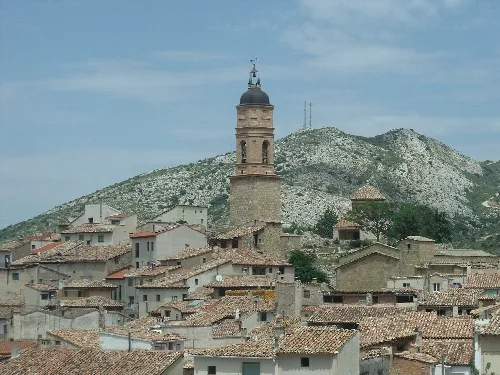 Blick auf eine Stadt mit Kirchturm und Häusern in einer bergigen Umgebung.