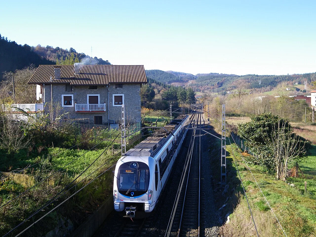 Moderner Zug auf Eisenbahnstrecken, umgeben von Häusern und Natur.