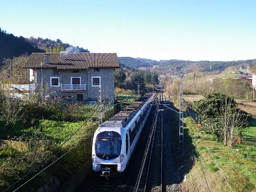 Tren moderno en vías ferroviarias rodeado de casas y naturaleza.