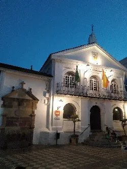 Edificio del ayuntamiento con banderas y una pila en la plaza de Ubrique.
