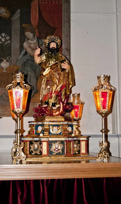 Statue of Saint Bartholomew with golden clothing and religious painting background.