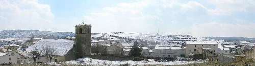 Landschaft mit Häusern und einem Turm in einem verschneiten Dorf.