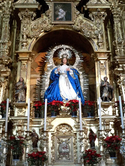 Statue der Jungfrau der Gnade auf einem goldenen Altar mit Figuren und roten Blumen.