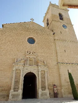 Fachada de una iglesia con torre y reloj en la plaza de Castalla.