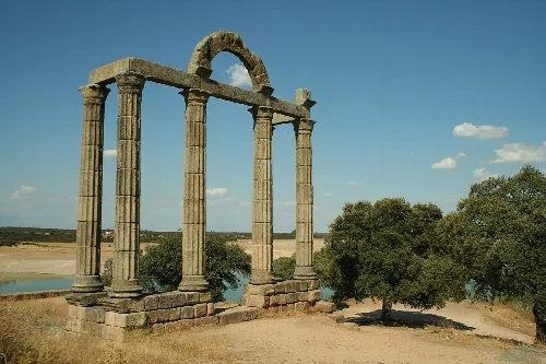 Granite colonnade with columns and arch in a rural landscape.