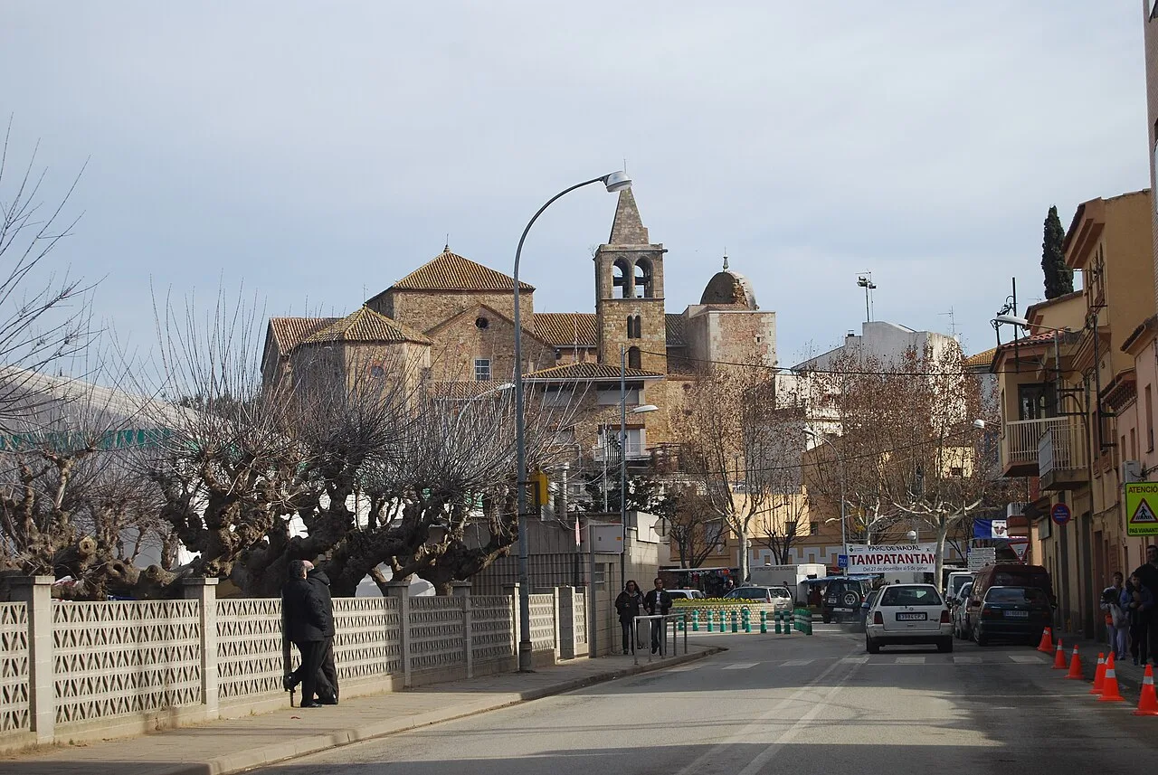 Vista de la calle con árboles, coches y la iglesia con campanario románico en el fondo.