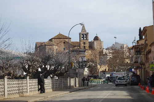 Straßenansicht mit Bäumen, Autos und der Kirche mit romanischem Glockenturm im Hintergrund.