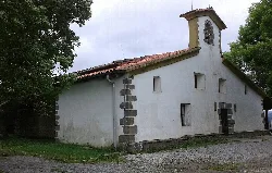 Iglesia blanca con campanario en una colina rodeada de árboles.