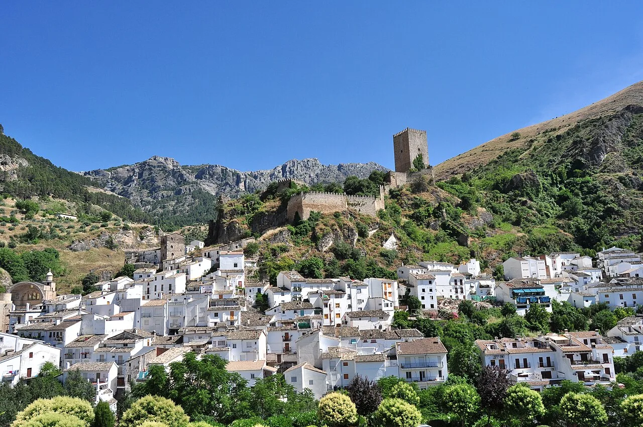 White houses and a tower on a hill with green mountains in the background.