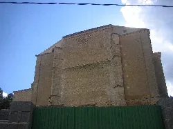 Parte posterior de una iglesia de piedra con cielo azul y nubes.