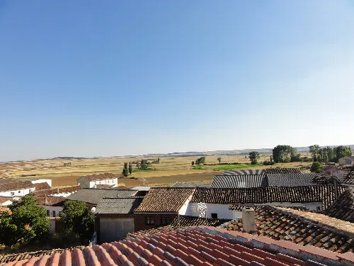 Fields and rooftops of Prádanos de Ojeda with clear blue sky.
