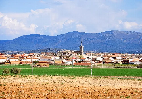 Landschaft mit Ort, Bergen und Feld im Vordergrund.