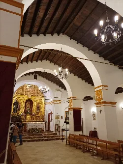 Vista del interior de una iglesia con arcos, candelabros y altar dorado.