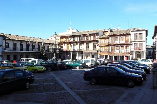 Plaza Mayor von La Puebla de Montalbán mit Gebäuden und geparkten Autos.