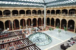 Patio interior con columnas, arcos y una estructura de vidrio en el centro.