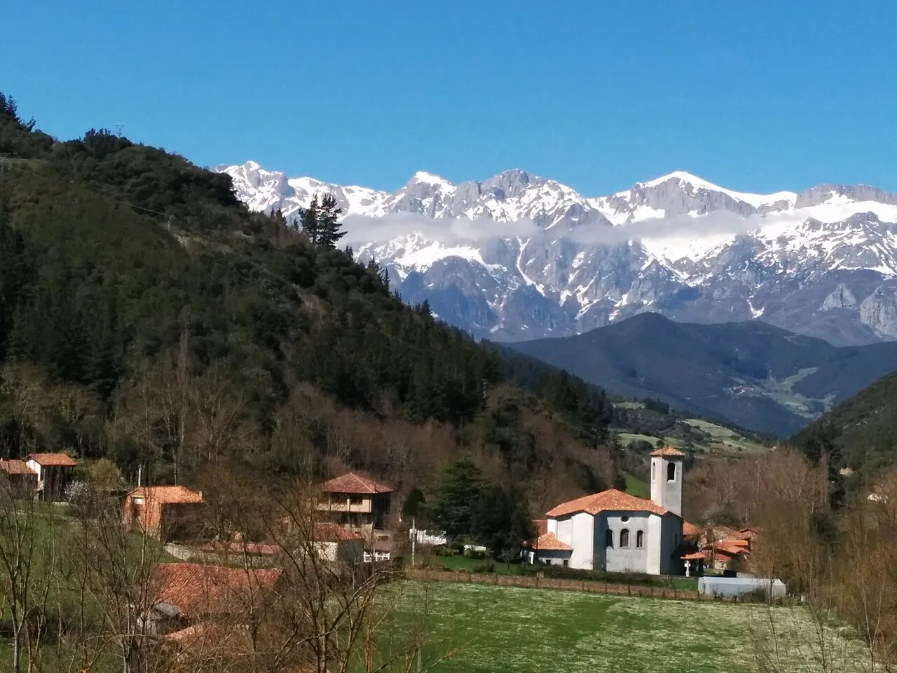 A village with houses and a church, with snow-capped mountains in the background.