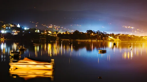 Boats on a river with reflections of lights and mountains in the background.