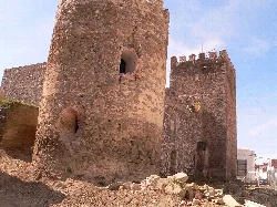 Torre redonda de piedra en un castillo con murallas y un cielo azul.