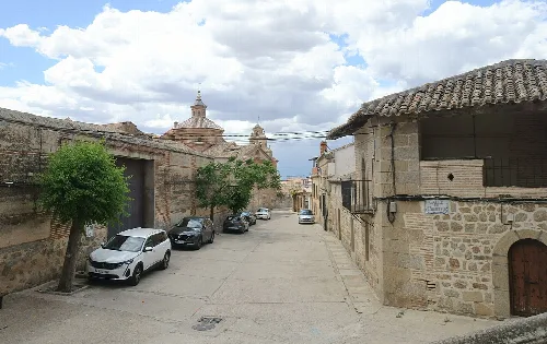 Straße mit Steinhäusern, Bäumen und geparkten Autos in La Calzada de Oropesa.