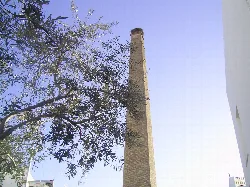 Hoher industrieller Schornstein mit Bäumen und Gebäude in Brenes.