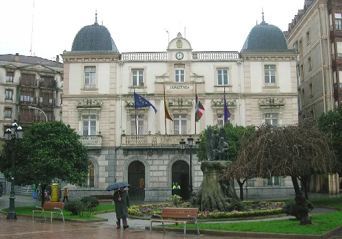 Edificio del ayuntamiento de Santurtzi con banderas y fuente en el parque.