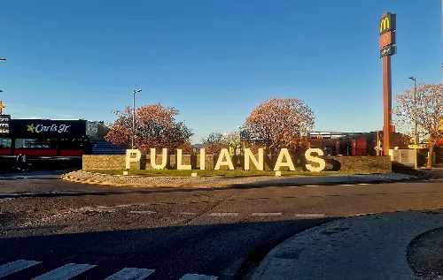 Pulianas-Schriftzug am Ortseingang mit Bäumen und einem Einkaufszentrum.