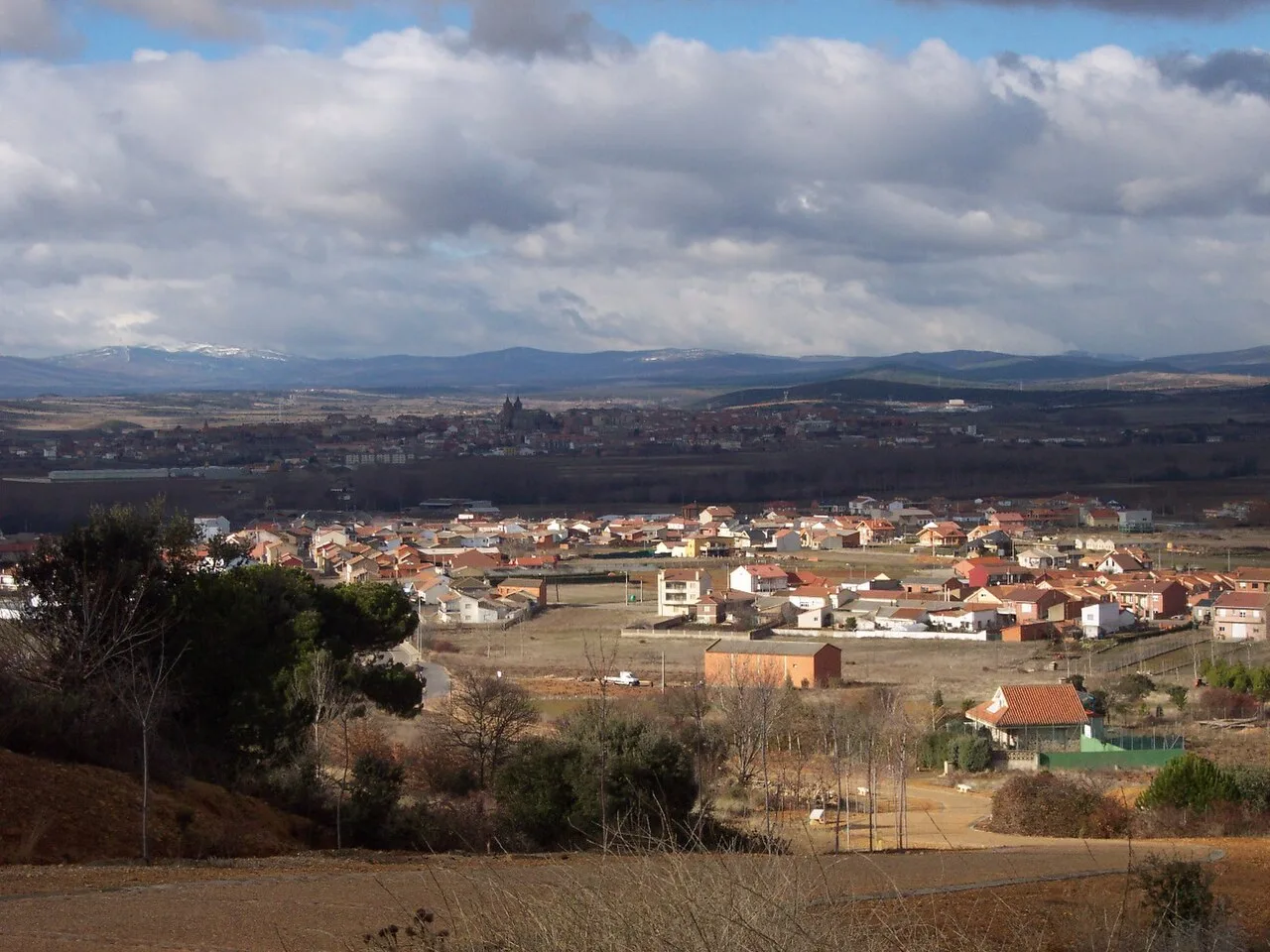 Paisaje con casas, campos y montañas bajo un cielo nublado.