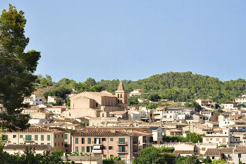 View of Sant Joan with houses and church in the center, surrounded by green hills.