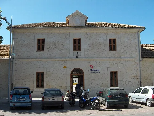 Bahnhof in Manacor mit geparkten Autos und Motorrädern vor dem Gebäude.