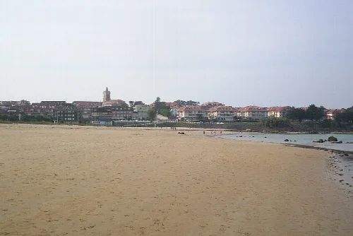 Amplia playa de arena con el pueblo y una iglesia en el horizonte.