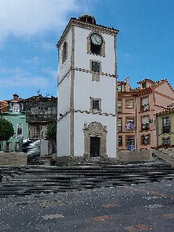 18th-century watchtower in Luanco with a clock at the top and colorful houses around.