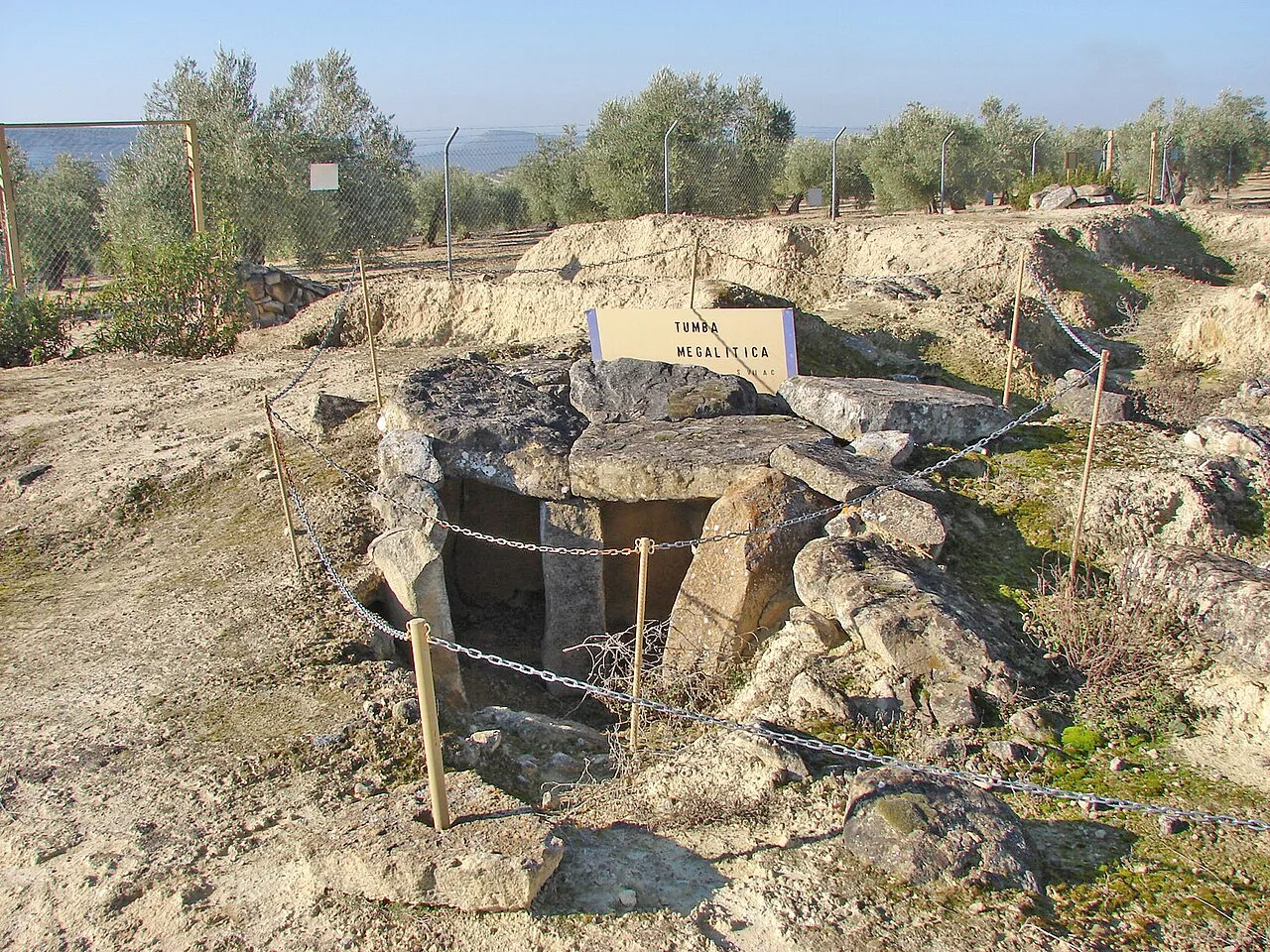Megalithic stone tomb at an archaeological site with signs and fencing.
