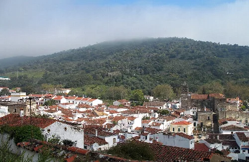 Blick auf weiße Häuser und eine Kirche in einer von grünen Hügeln umgebenen Stadt.