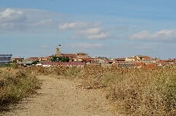 Vista de un pueblo con casas y una iglesia en el centro, bajo un cielo con nubes.