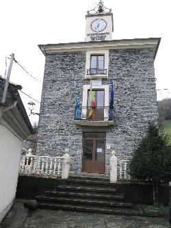 Edificio de piedra con reloj y banderas en Villanueva de Oscos.