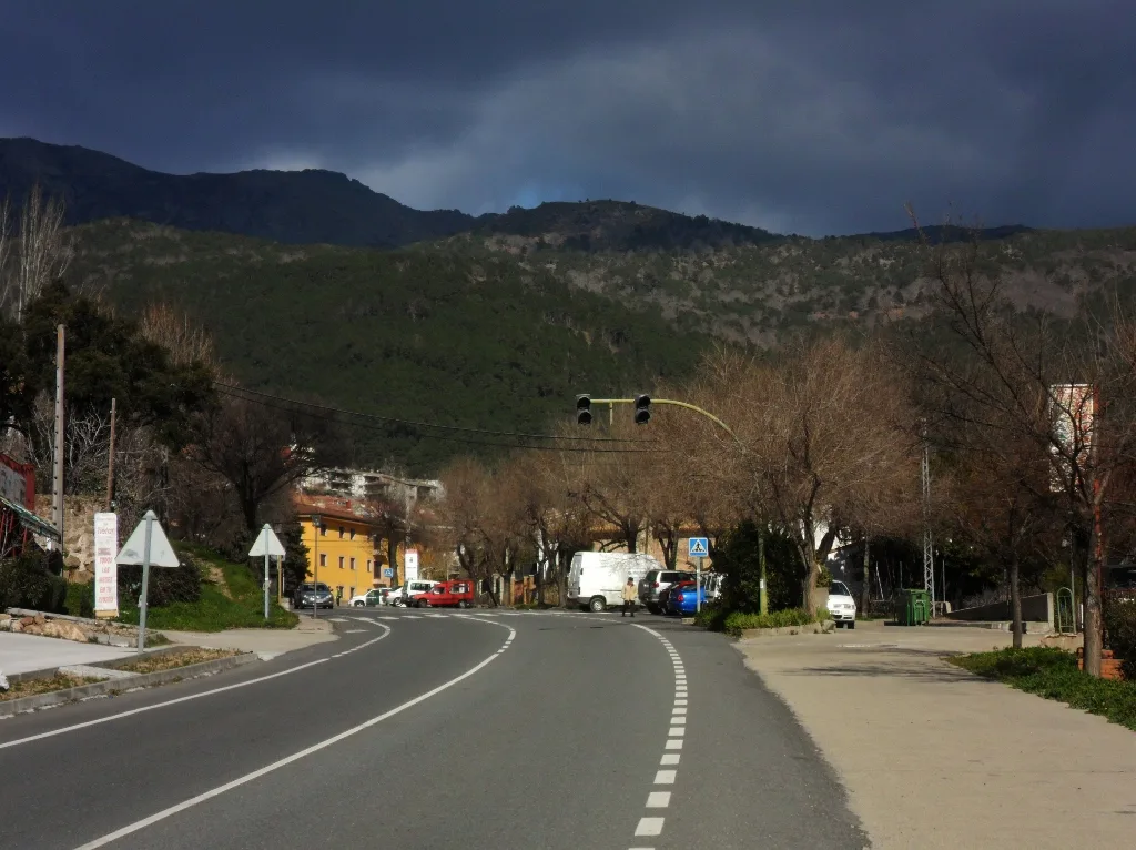 Vista de la calle principal de Piedralaves con montañas al fondo y árboles sin hojas.