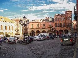 Square with old buildings and parked cars.