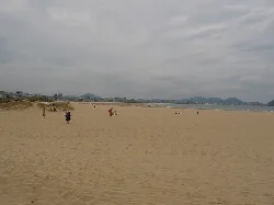 Weitläufiger Strand mit Sand und wenigen Menschen, bewölkter Himmel.