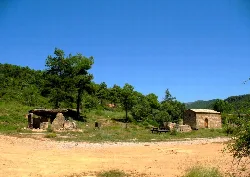 Dolmen de piedra y ermita en un paisaje con árboles y cielo azul en La Baronia de Rialb.