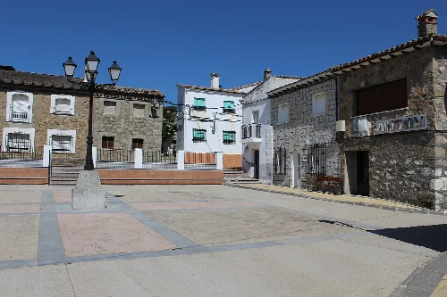 Square with lampposts, stone buildings, and a blue sky in Sartajada.