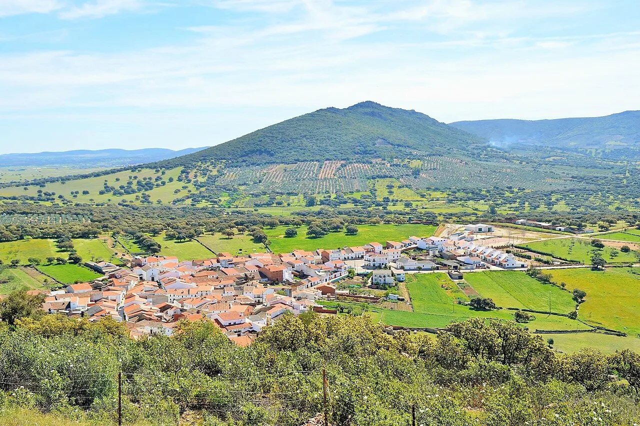 Vista de Tamurejo con casas, campos verdes y una colina en el fondo.