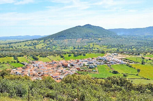 Panoramic view of Tamurejo with houses, green fields, and a hill in the background.