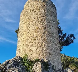 Runder Steinturm in einer Landschaft mit blauem Himmel und Vegetation.