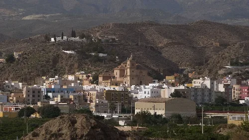 Vista de Gádor con edificios, iglesia y montañas en el fondo.