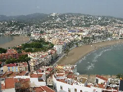 Vista aérea de playas y edificios en Peñíscola con colina y castillo en la distancia.