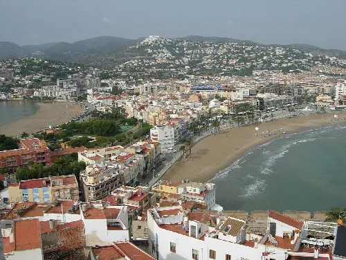 Vista aérea de playas y edificios en Peñíscola con colina y castillo en la distancia.