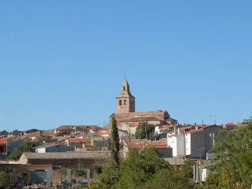 Vista de un pueblo con iglesia y tejados en otoño bajo cielo azul.