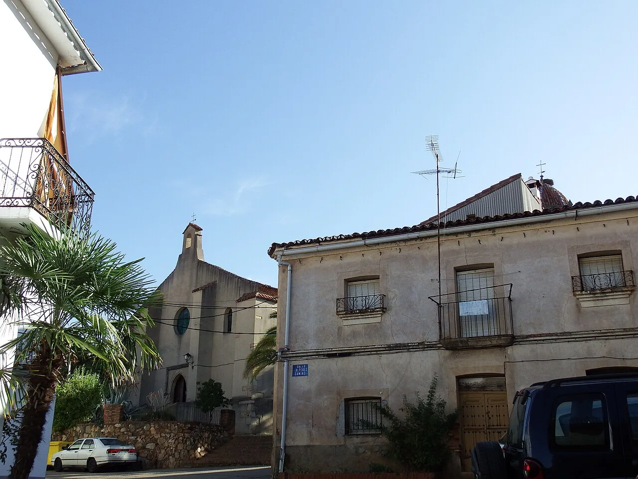 Casas y palmeras en Cañamero, con iglesia visible en el fondo.