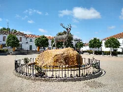 Hirschstatue auf einem Platz mit Bäumen und weißen Gebäuden in El Real de la Jara.