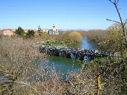 Puente de piedra sobre el río Zadorra, con iglesia y casas en el fondo.